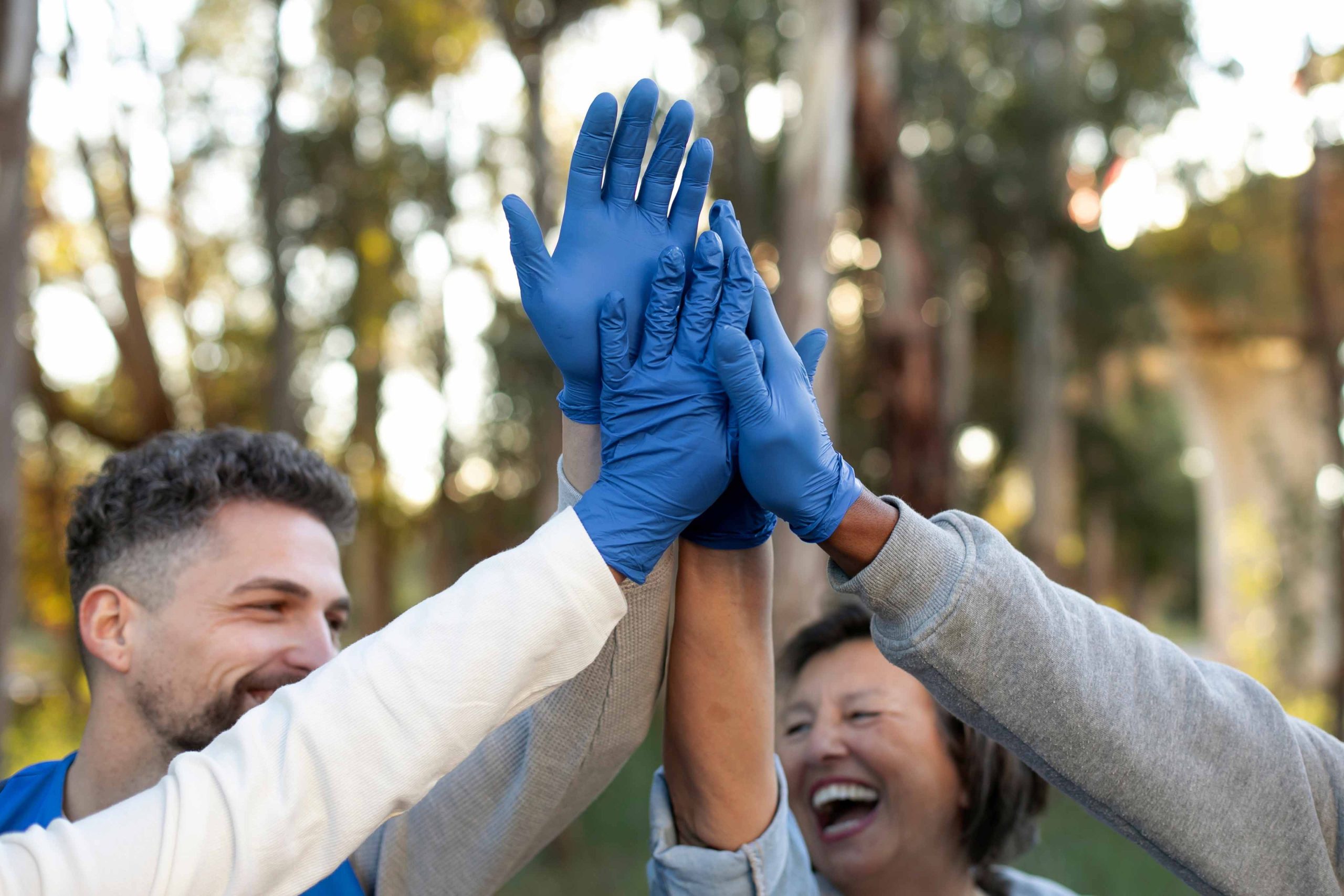 Grupo de personas levantando las manos con guantes azules en un ambiente alegre.